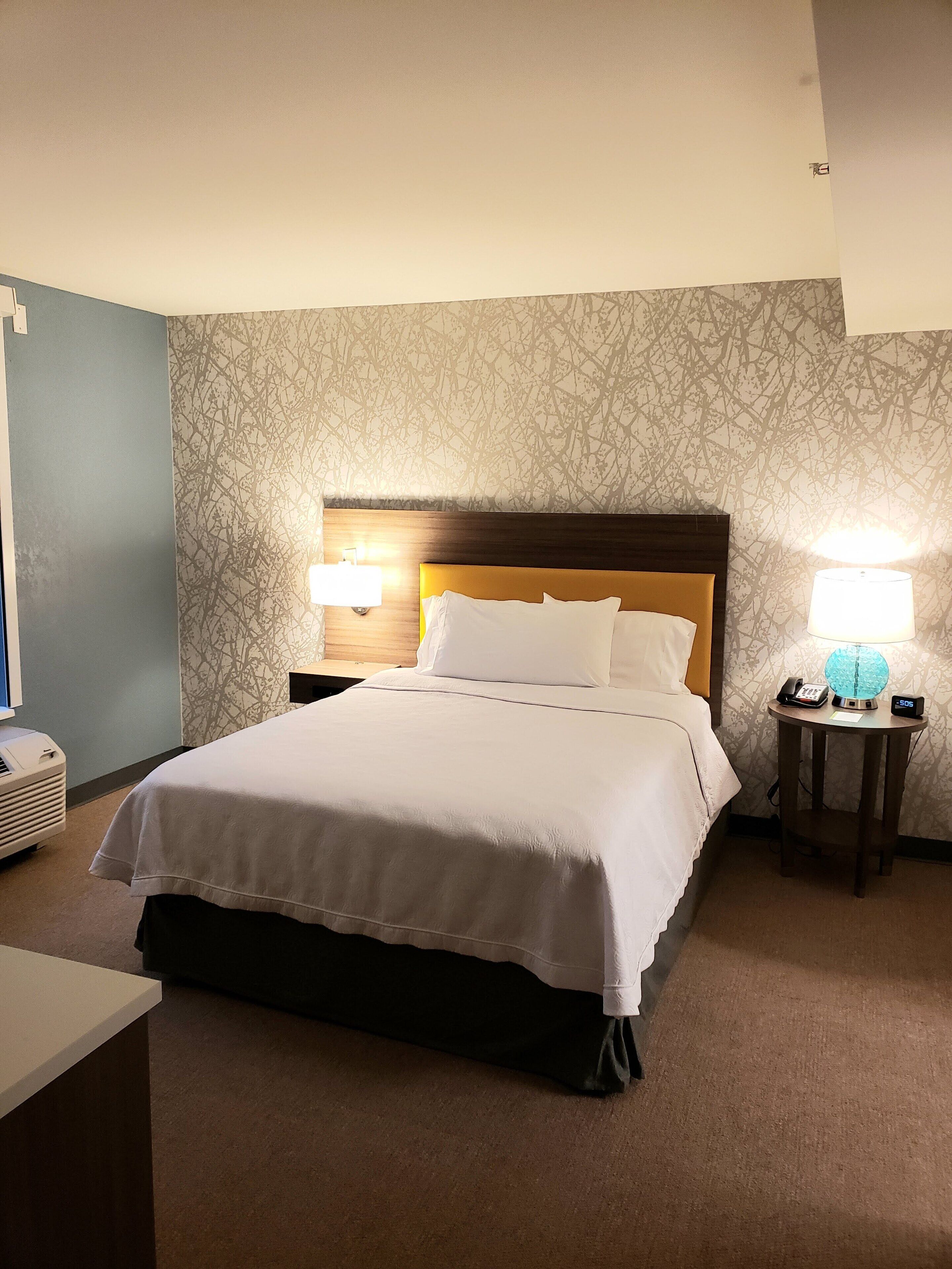 Habitación de hotel con una cama grande, dos lámparas de noche, un teléfono en la mesita y un calentador de pared.