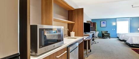 Una habitación de hotel moderna con kitchenette, una cama, un escritorio y una silla.