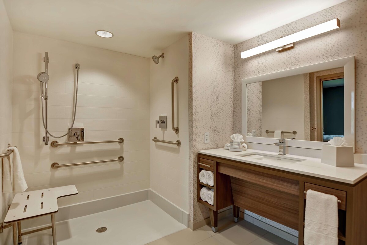 Een moderne badkamer met een inloopdouche, grepen, een wastafel met spiegel en een handdoekrek.