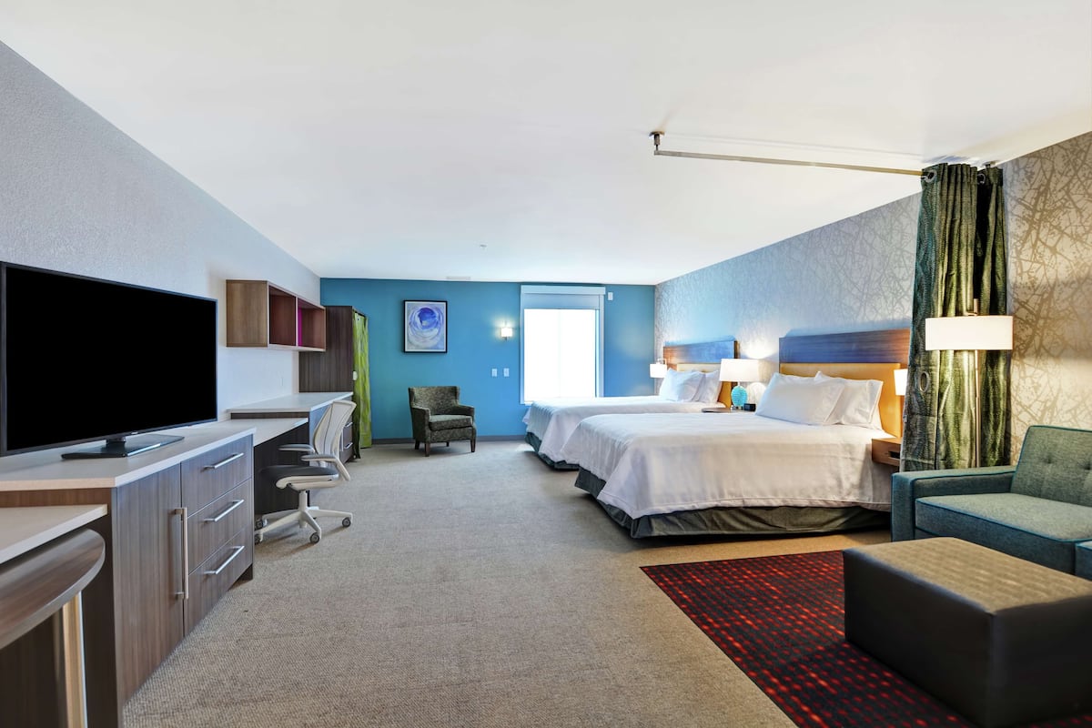 Una habitación de hotel con escritorio, televisor, dos camas, una silla y un sofá.