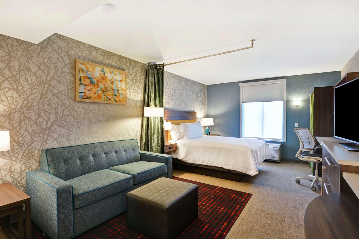 Een hotelkamer met een bed, een slaapbank, een bureau, een televisie en een schilderij aan de muur.