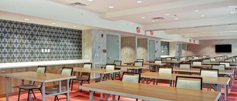 A conference room with multiple tables and chairs, a patterned wall, and a television screen.