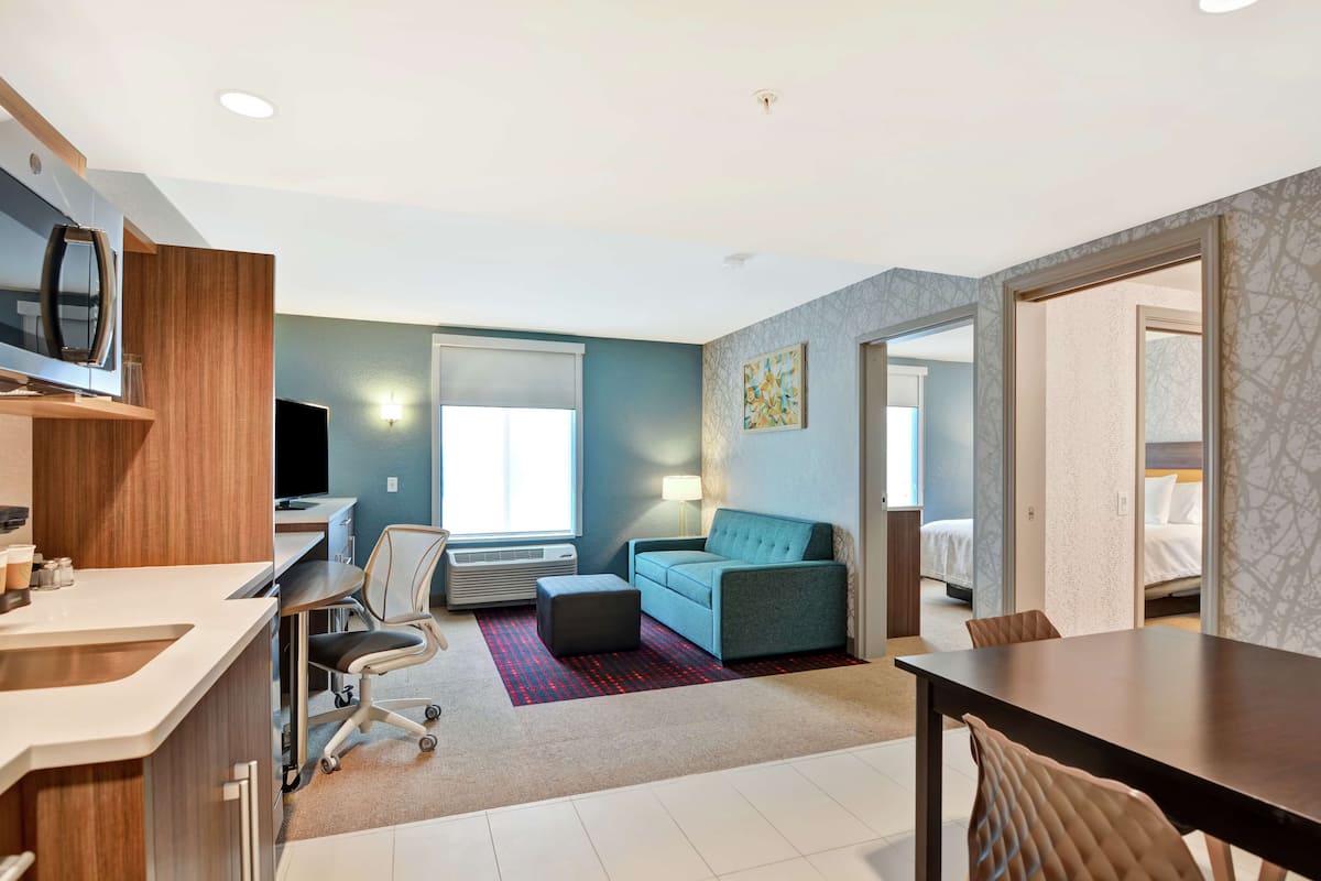 Una habitación de hotel moderna con kitchenette, un sofá, una mesa de comedor y una cama.
