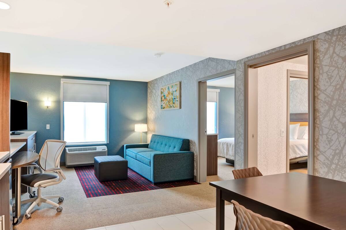 Una habitación de hotel moderna con escritorio, silla, sofá y mesa de comedor.