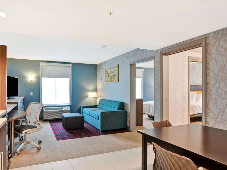 A modern hotel room with a desk, chair, sofa, and a dining table.