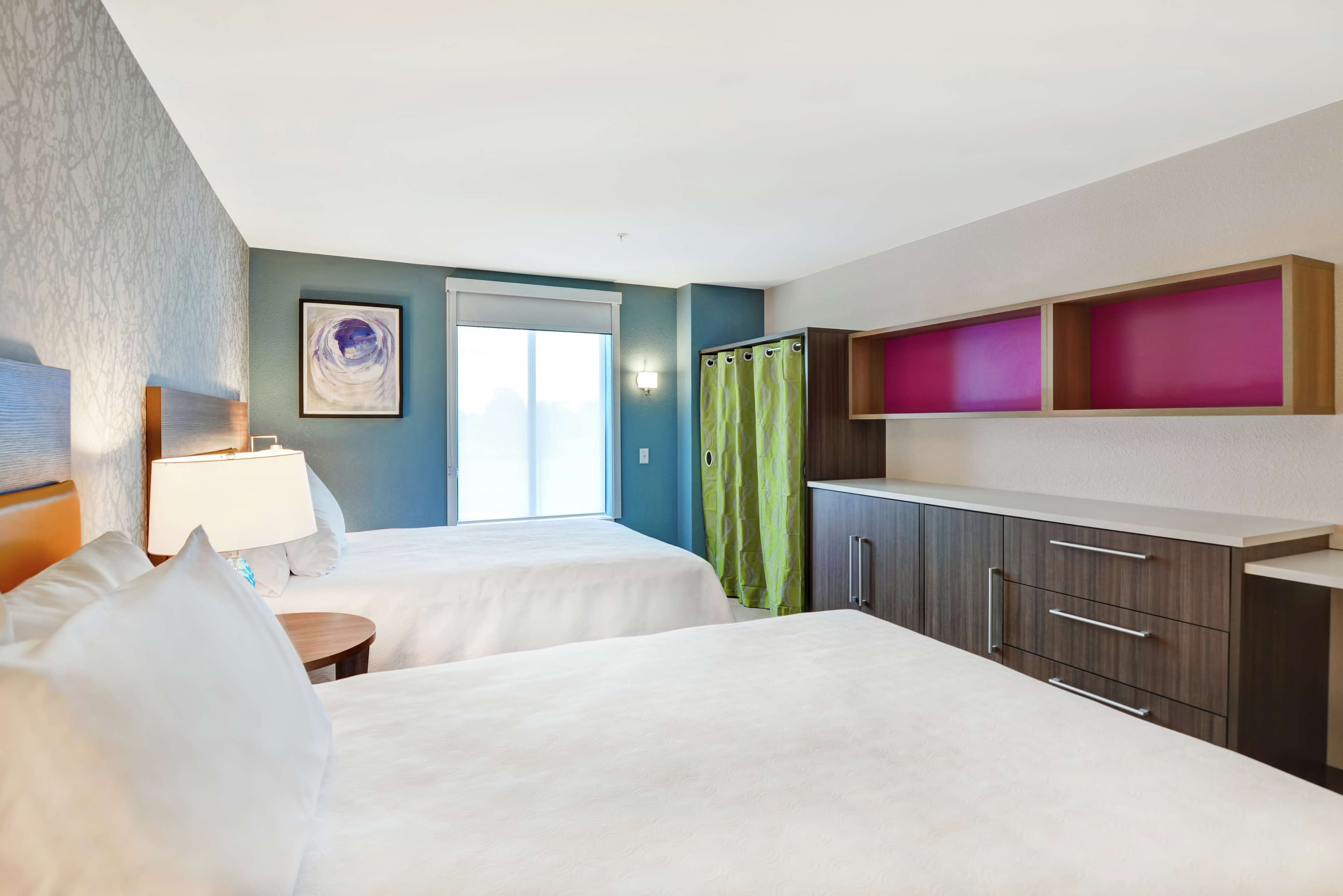 Habitación de hotel con dos camas, una ventana con vistas, una cortina verde y un armario con cajones.