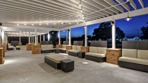 Un espace de détente extérieur doté de différents types de sièges, notamment des canapés et des bancs, aménagé sous une structure couverte avec un plafond en forme de treillis.