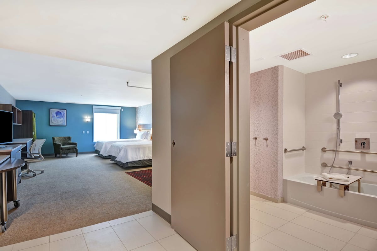 Habitación de hotel con baño, escritorio, silla, cama y vista a otra habitación.