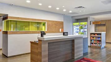A hotel reception desk with a glass partition, a minibar, and a self-service kiosk.