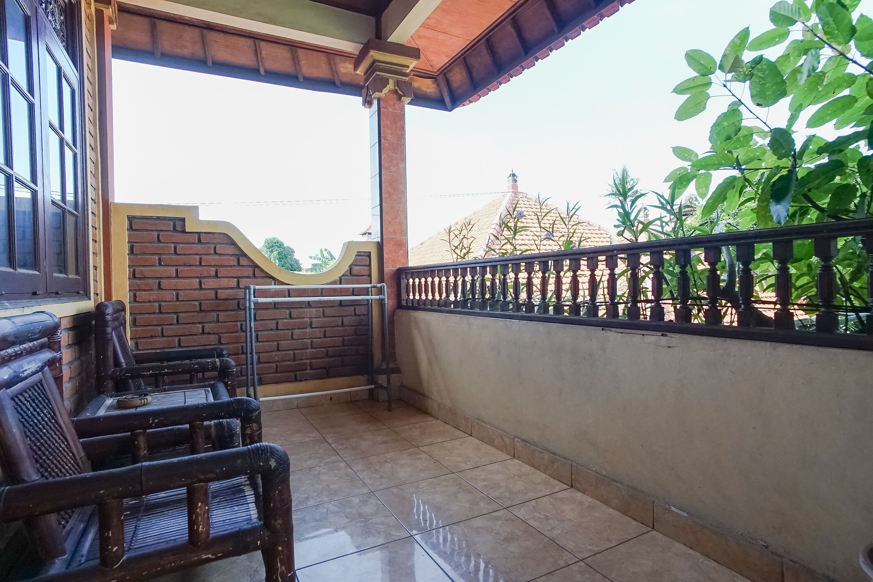 A covered outdoor area with a tiled floor, a brick wall, a metal railing, and a wooden bench.