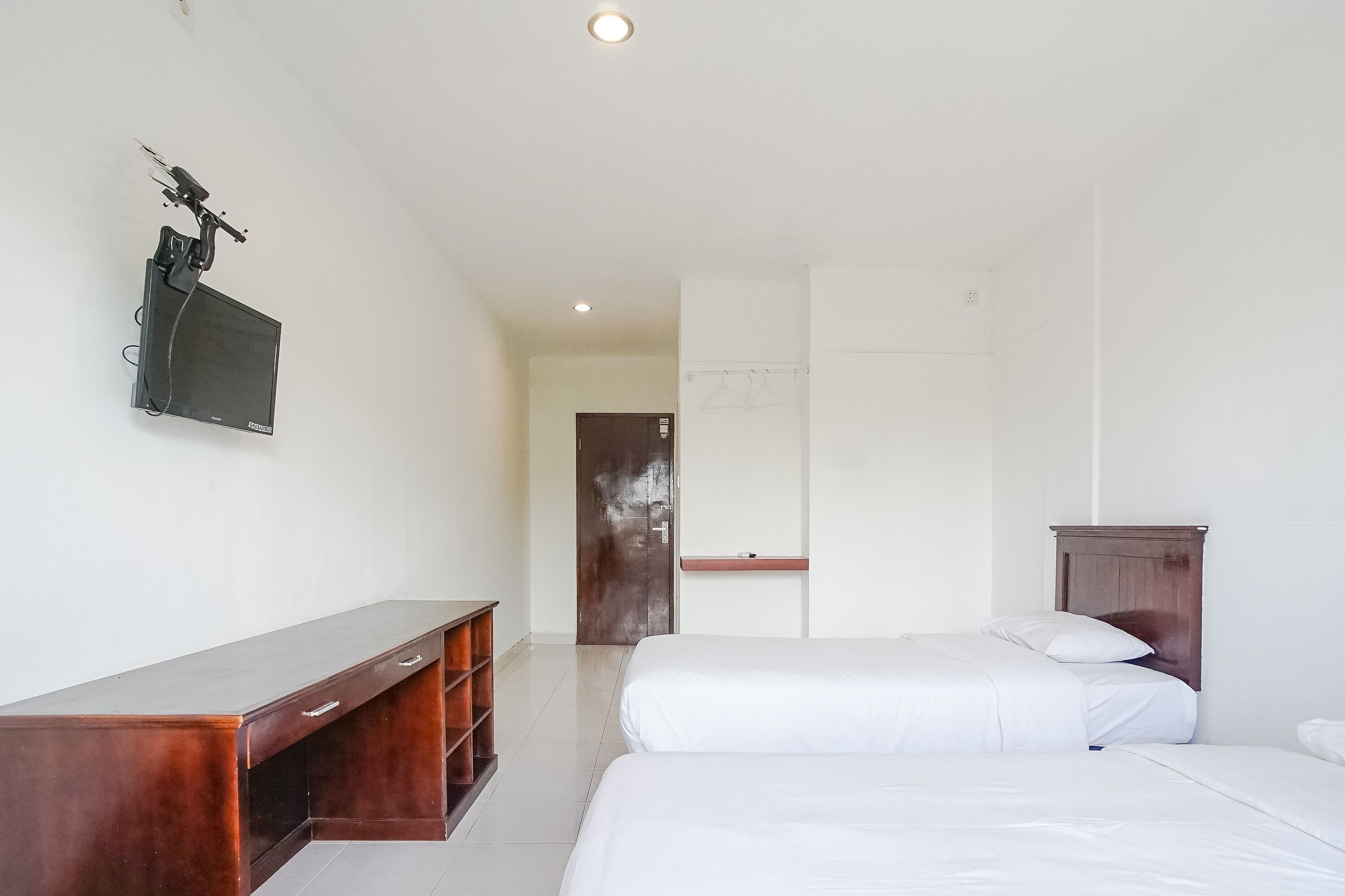 A hotel room with a wooden desk, a bed, a wardrobe, and a television mounted on the wall.