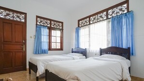 Quarto com duas camas de solteiro, cabeceiras de madeira e uma porta grande de madeira.