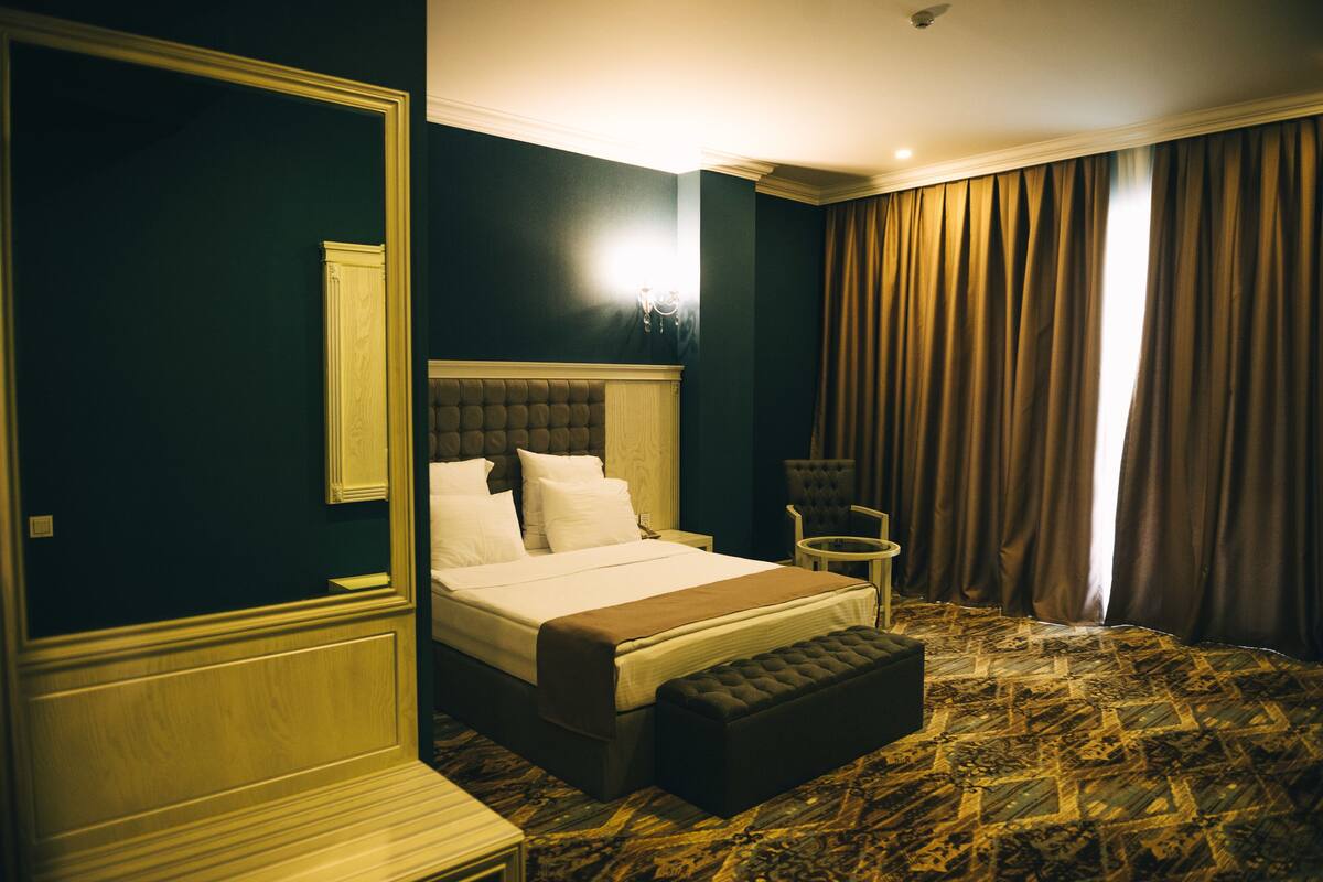 A hotel room with a large bed, a bench, a small table, and a chair.