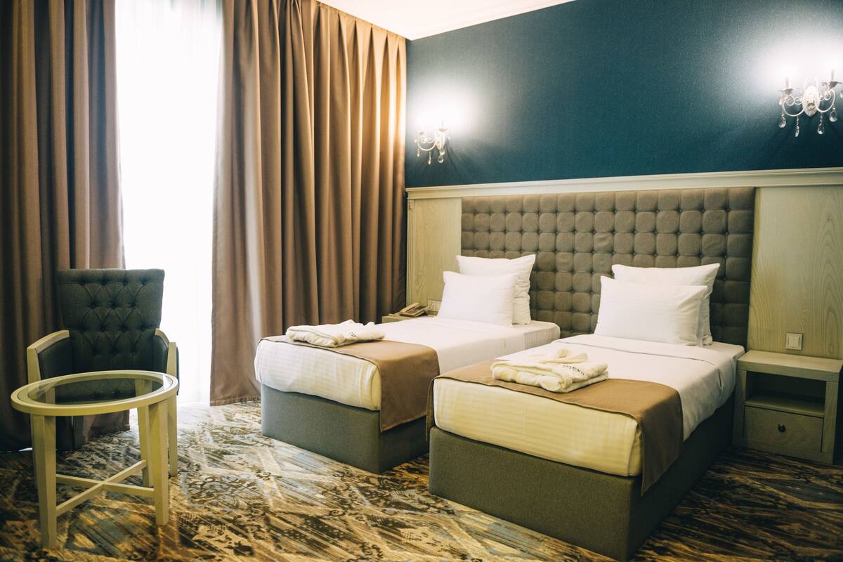 A hotel room with two beds, a small table, a chair, and a nightstand.