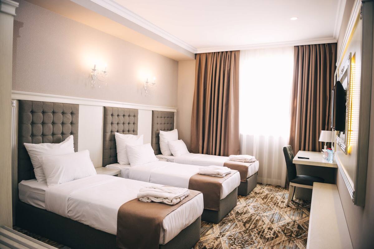 A hotel room with three beds, a desk, and a chair.