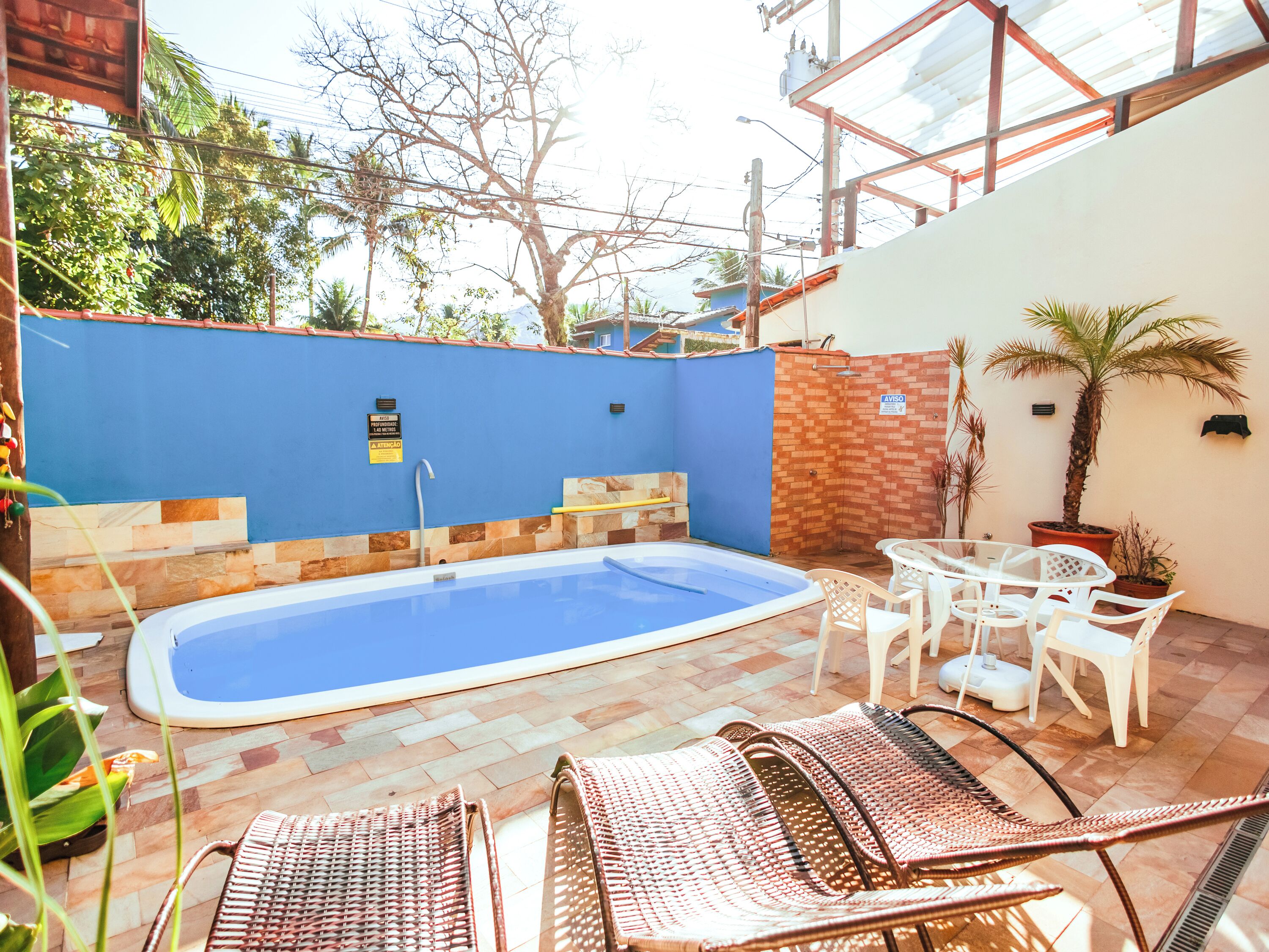 Una piscina con solárium de baldosas, rodeada de sillas de mimbre y una pequeña mesa.