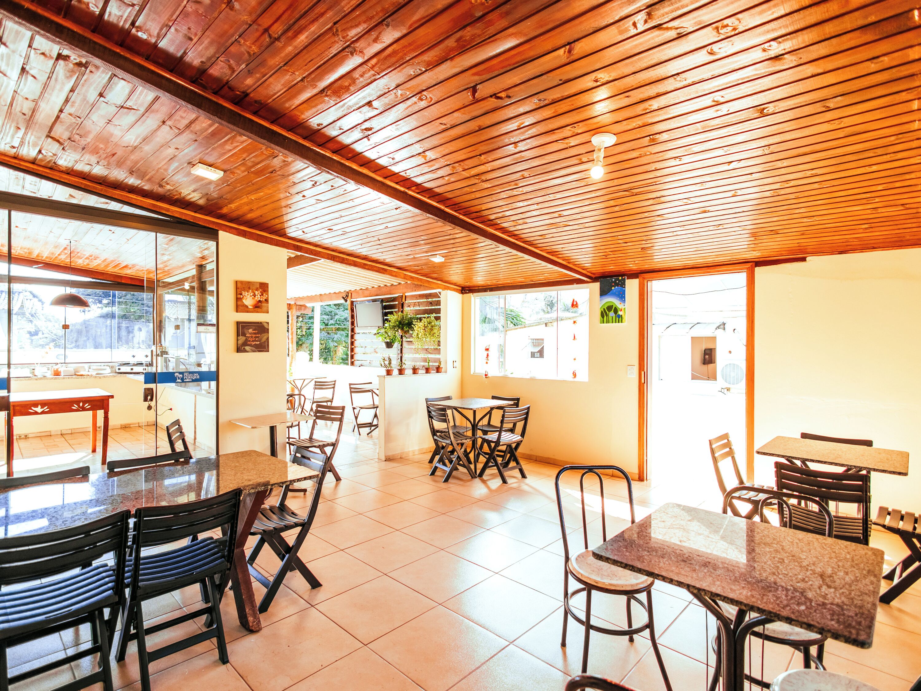 A restaurant with wooden ceiling beams, tiled floor, and multiple tables and chairs.