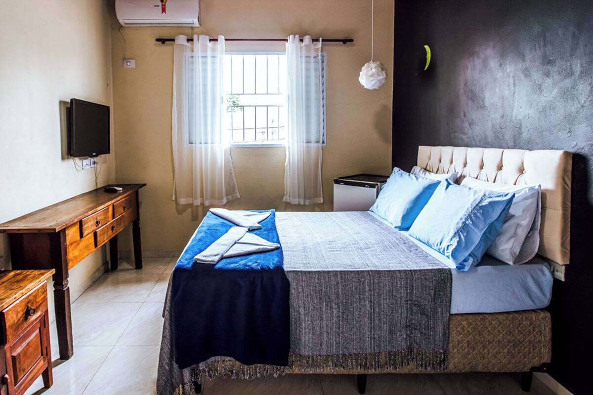 A bedroom with a bed, a television, a desk, and a window with curtains.