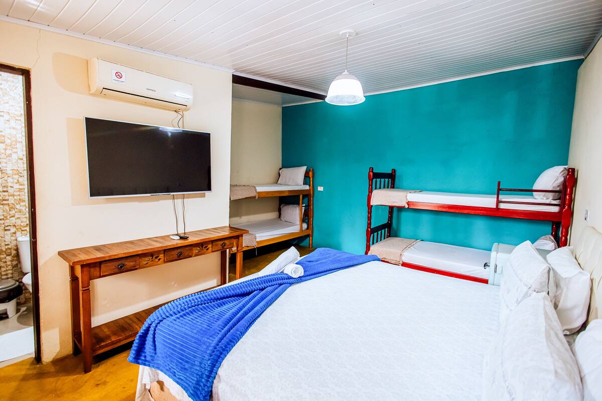 A room with a bed, a TV, a bench, and bunk beds.