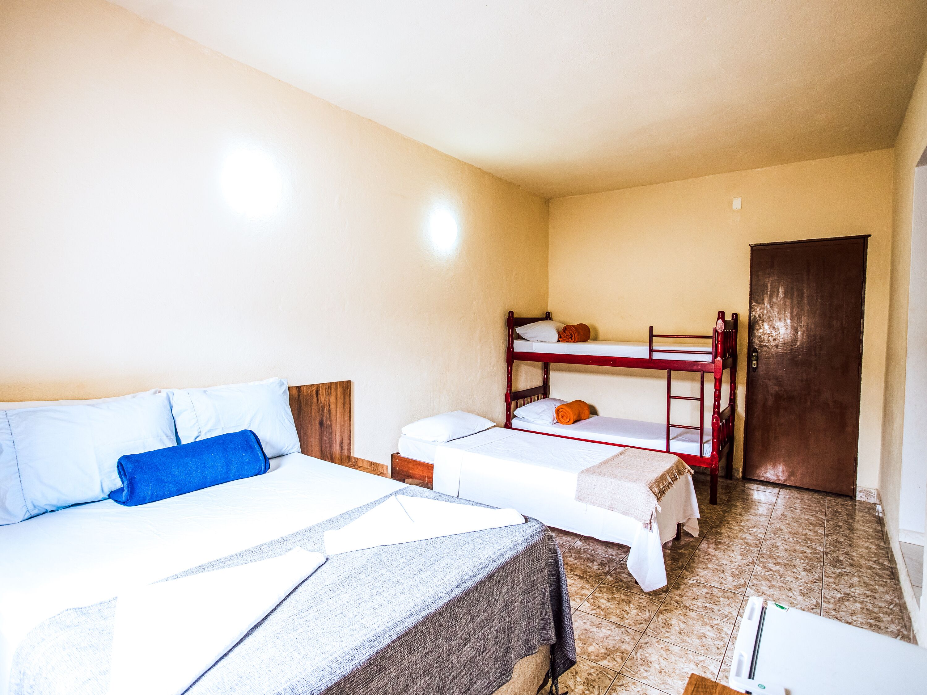 Habitación tipo dormitorio con dos camas individuales y una litera, una puerta y suelo de baldosas.