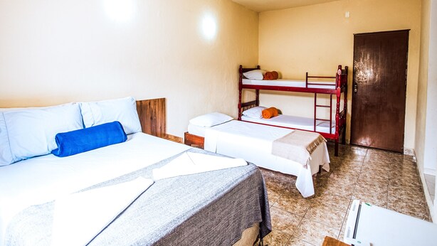 A dormitory room with two single beds and a bunk bed, a door, and a tiled floor. - VELINN Pousada Praia do Perequê (Ilhabela)