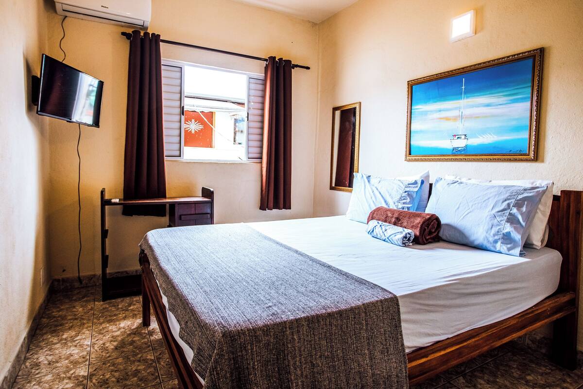 A hotel room with a bed, a desk, a TV, and a painting on the wall.