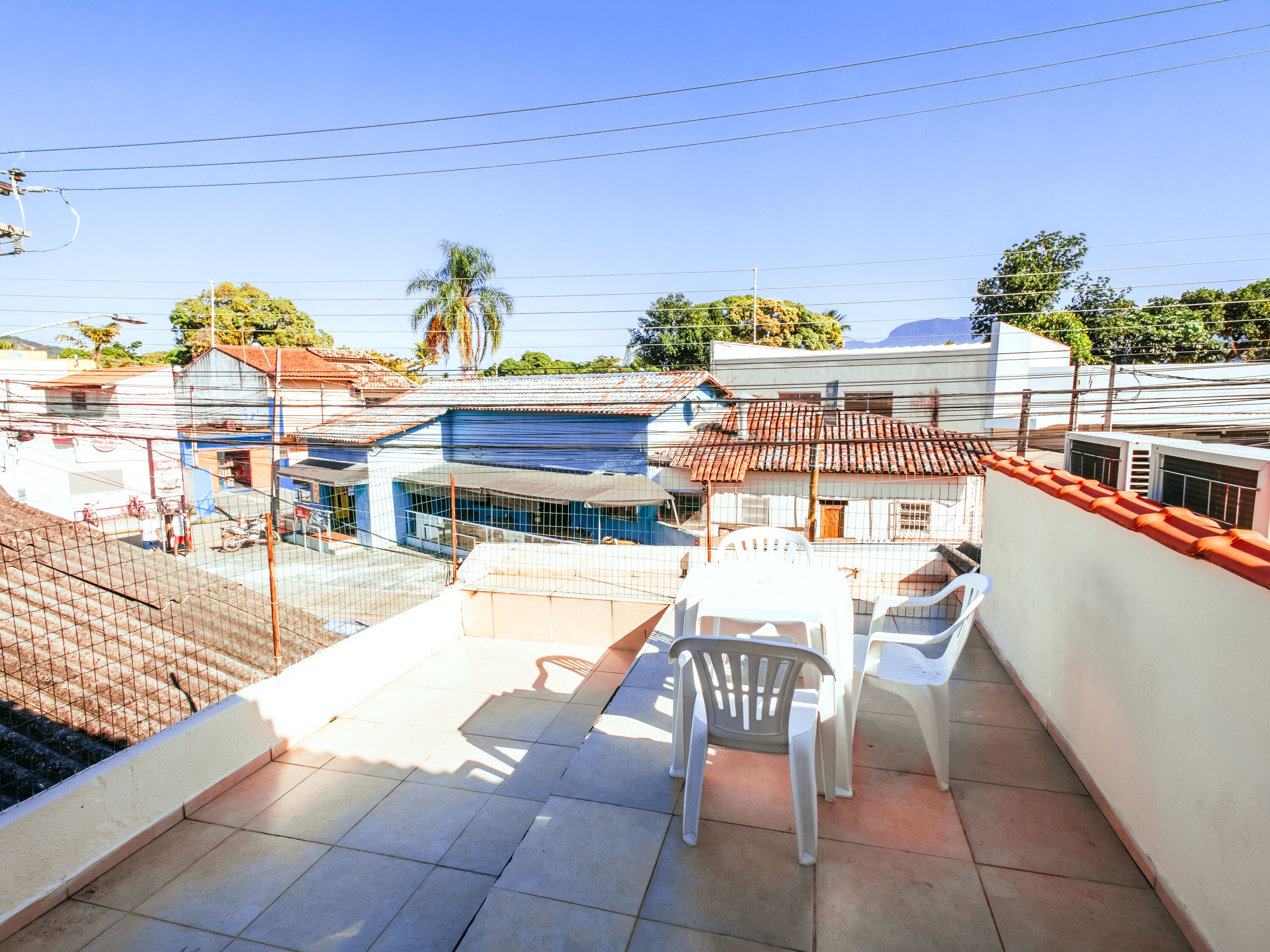 A rooftop terrace with tiled flooring, white plastic chairs, and a view of surrounding buildings.