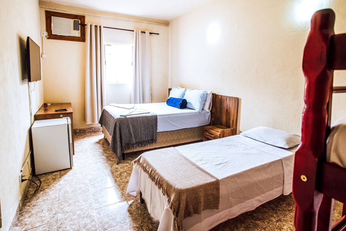 A hotel room with two beds, a small table, a TV, and a window with curtains.