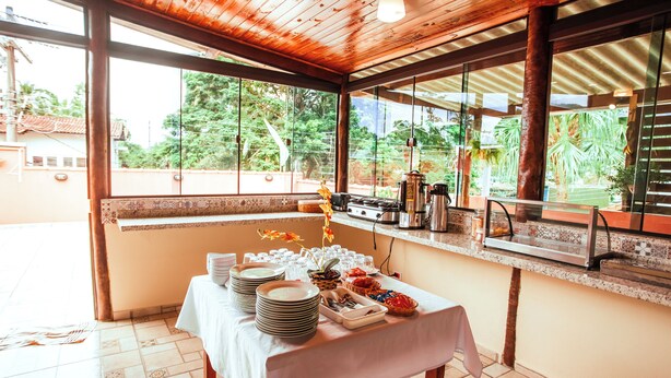 A dining area with a table set for a meal, a coffee station, and a view of greenery outside. - VELINN Pousada Praia do Perequê (Ilhabela)