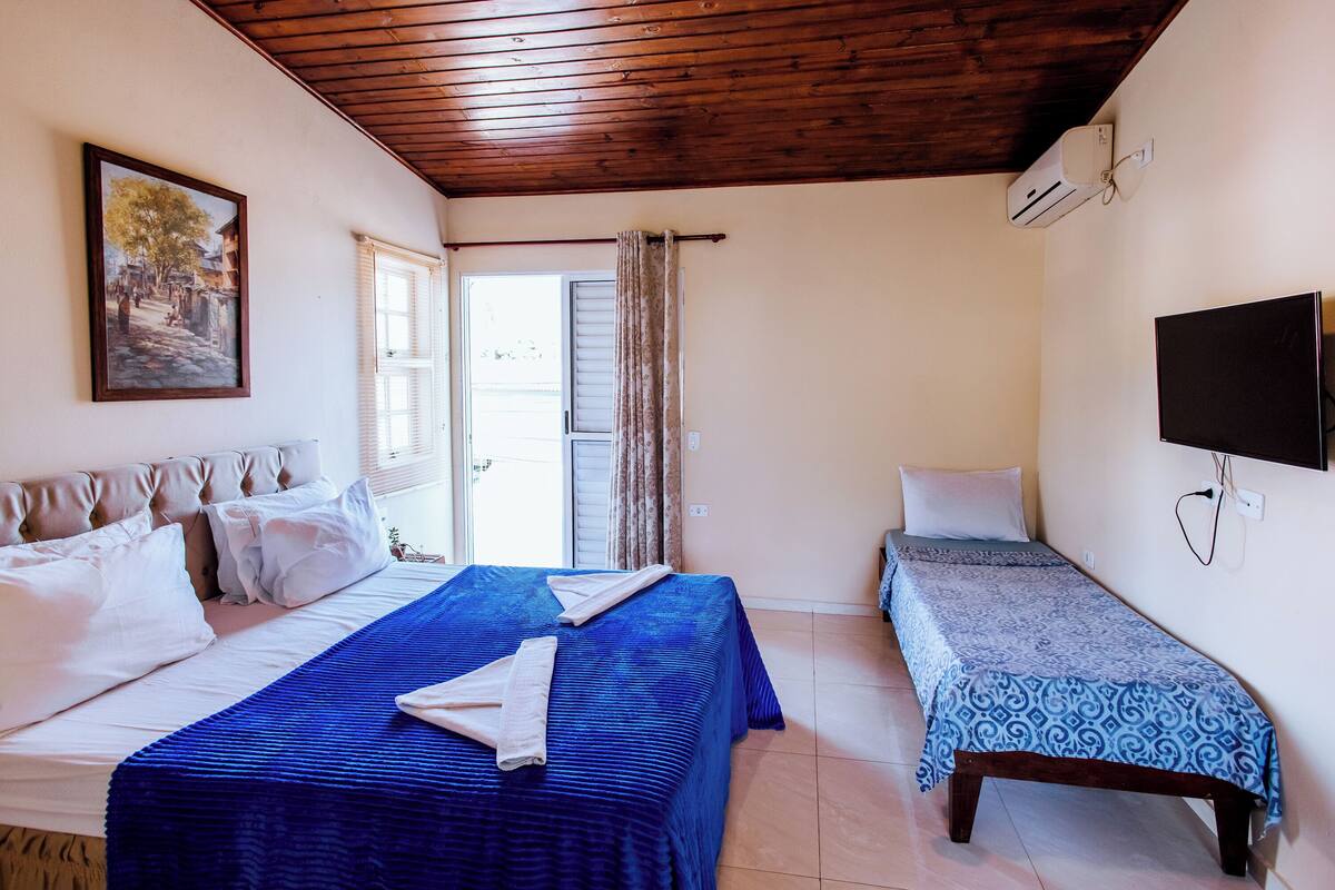 A bedroom with a bed, a smaller bed, a TV, and a painting on the wall.