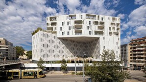 A modern building with a unique perforated facade and multiple balconies.