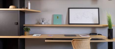 Un espacio de trabajo moderno con un escritorio de madera, una silla de mimbre y estanterías con varios objetos, incluyendo una planta, una botella de agua y un boceto enmarcado.