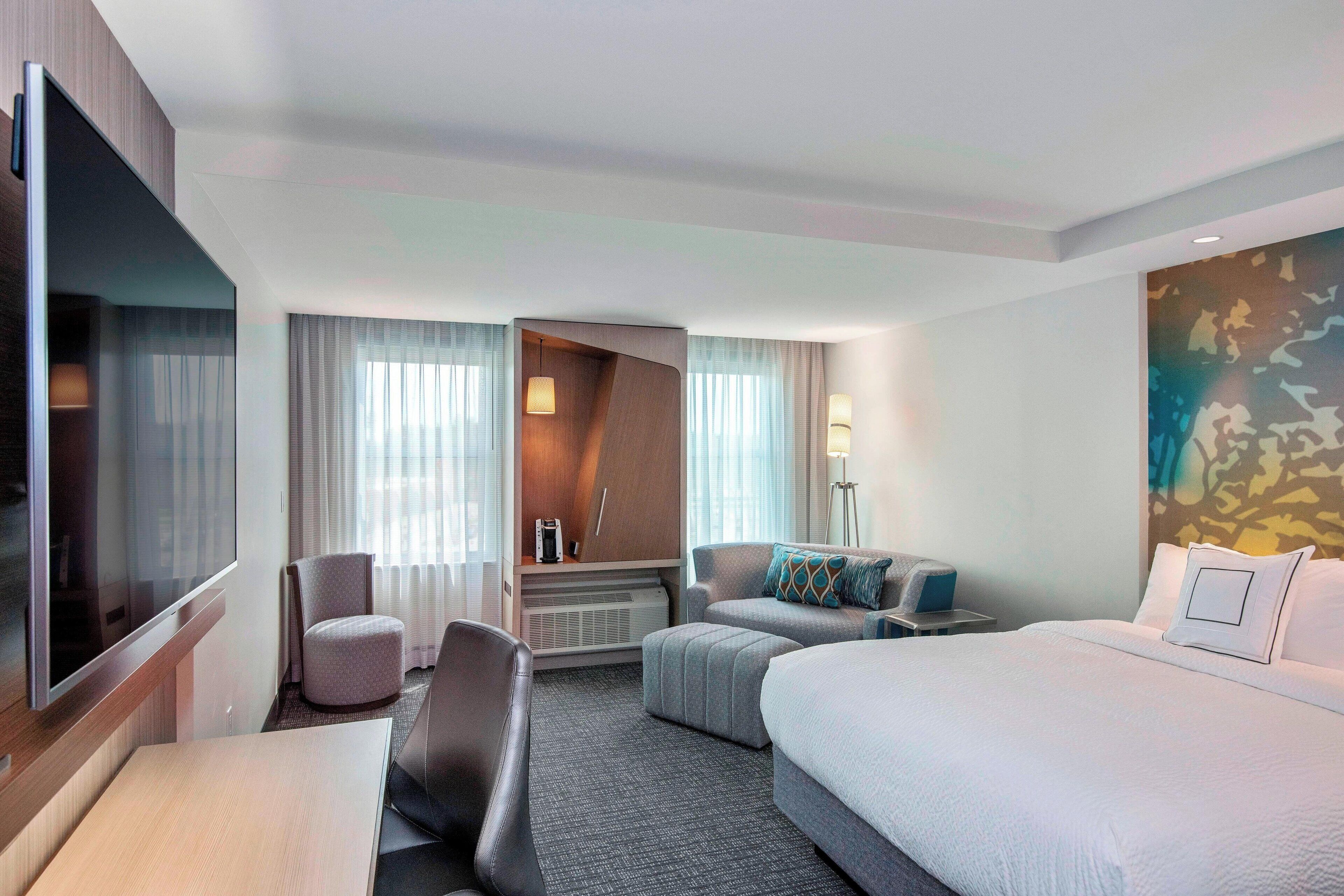 A hotel room with a bed, a desk, a chair, a sofa, and a TV.