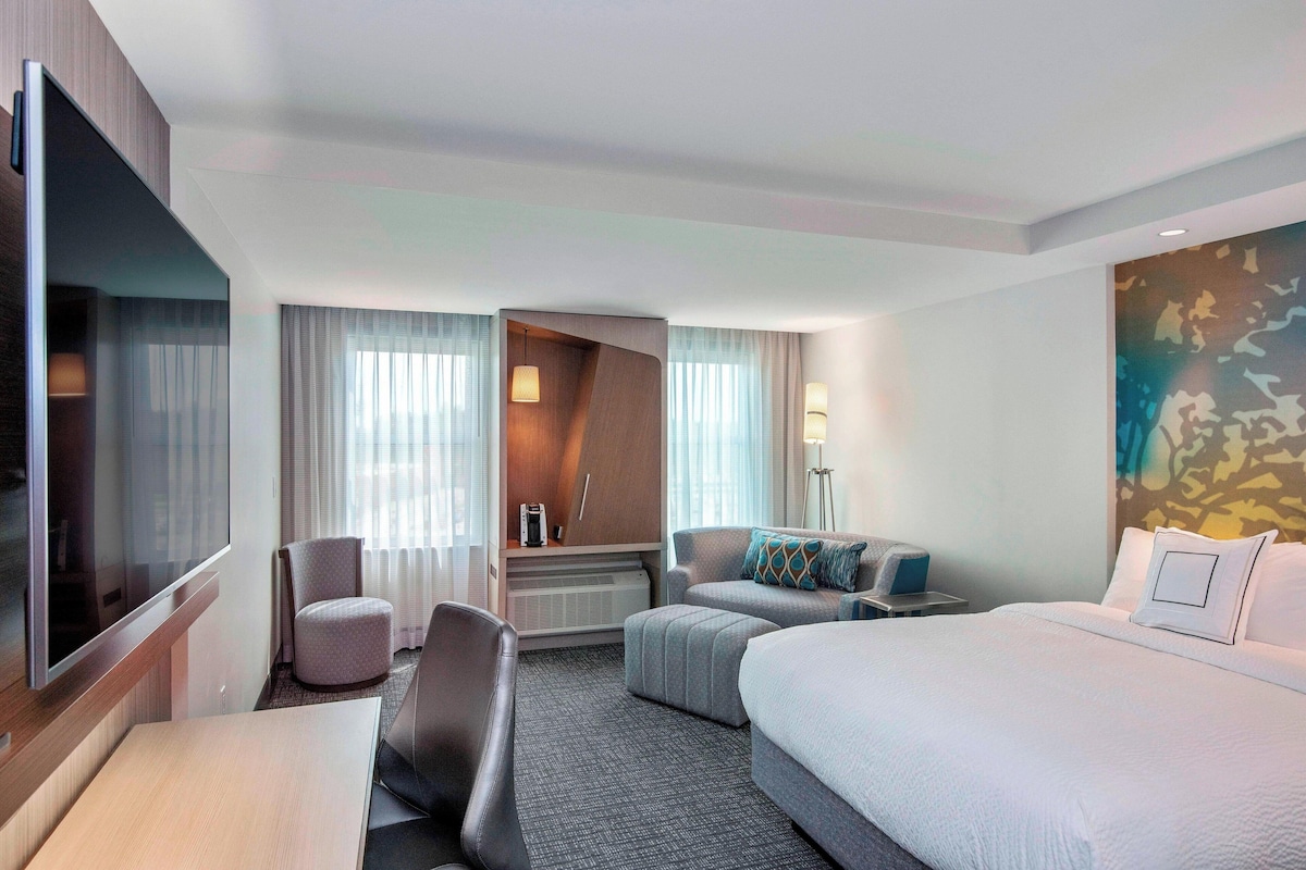 A hotel room with a bed, a desk, a chair, a sofa, and a TV.