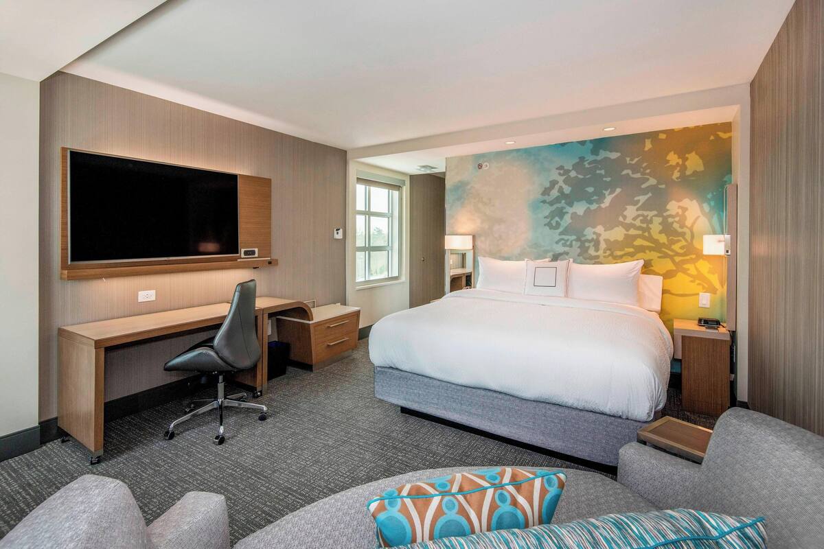 A hotel room with a large bed, a desk with a chair, a television, and a painting on the wall.
