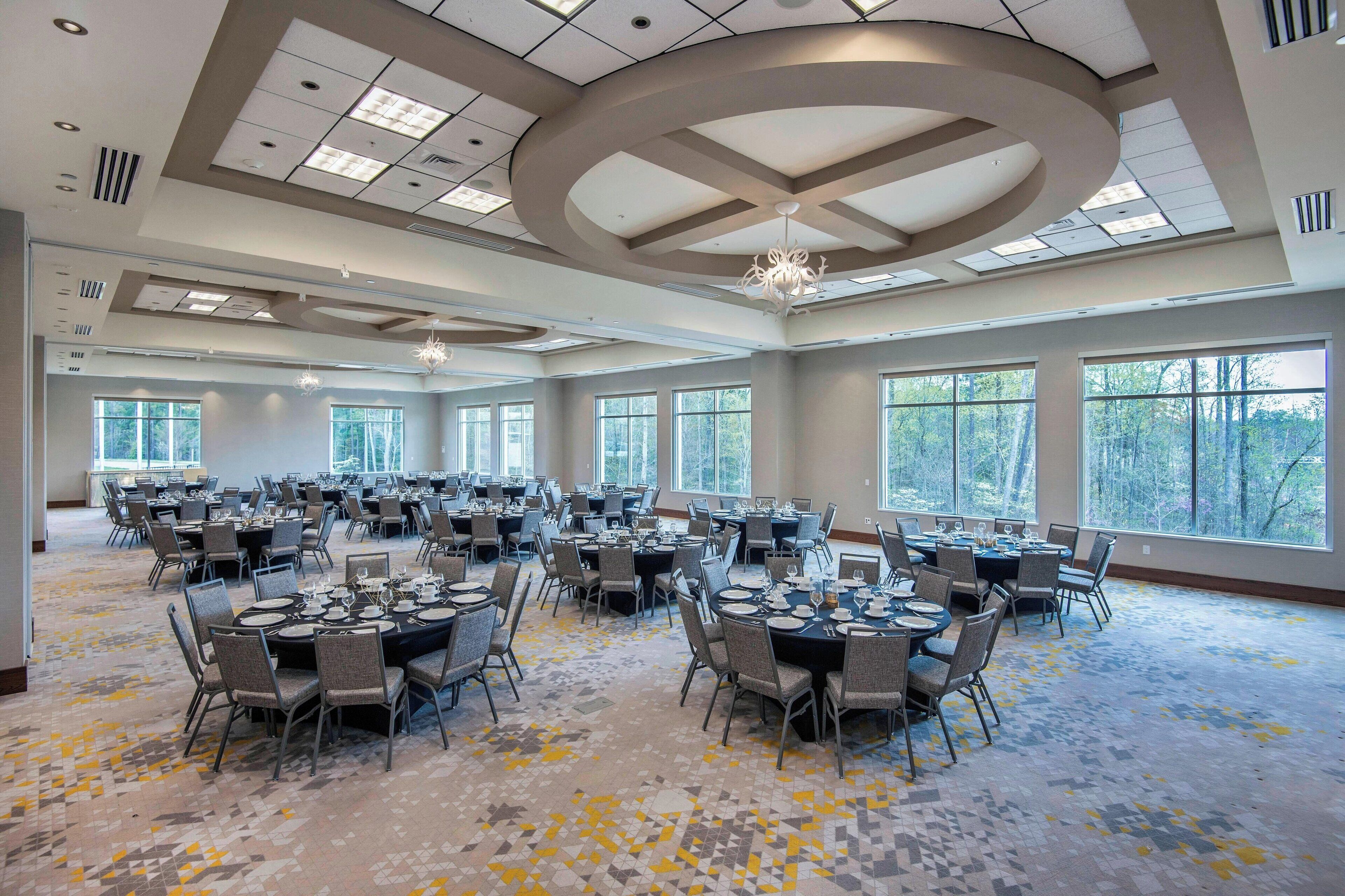 A large conference room with multiple tables and chairs, large windows, and a patterned carpet.