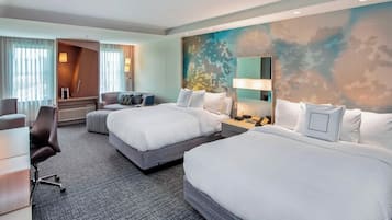 A hotel room with two beds, a desk, a chair, and a large window with curtains.