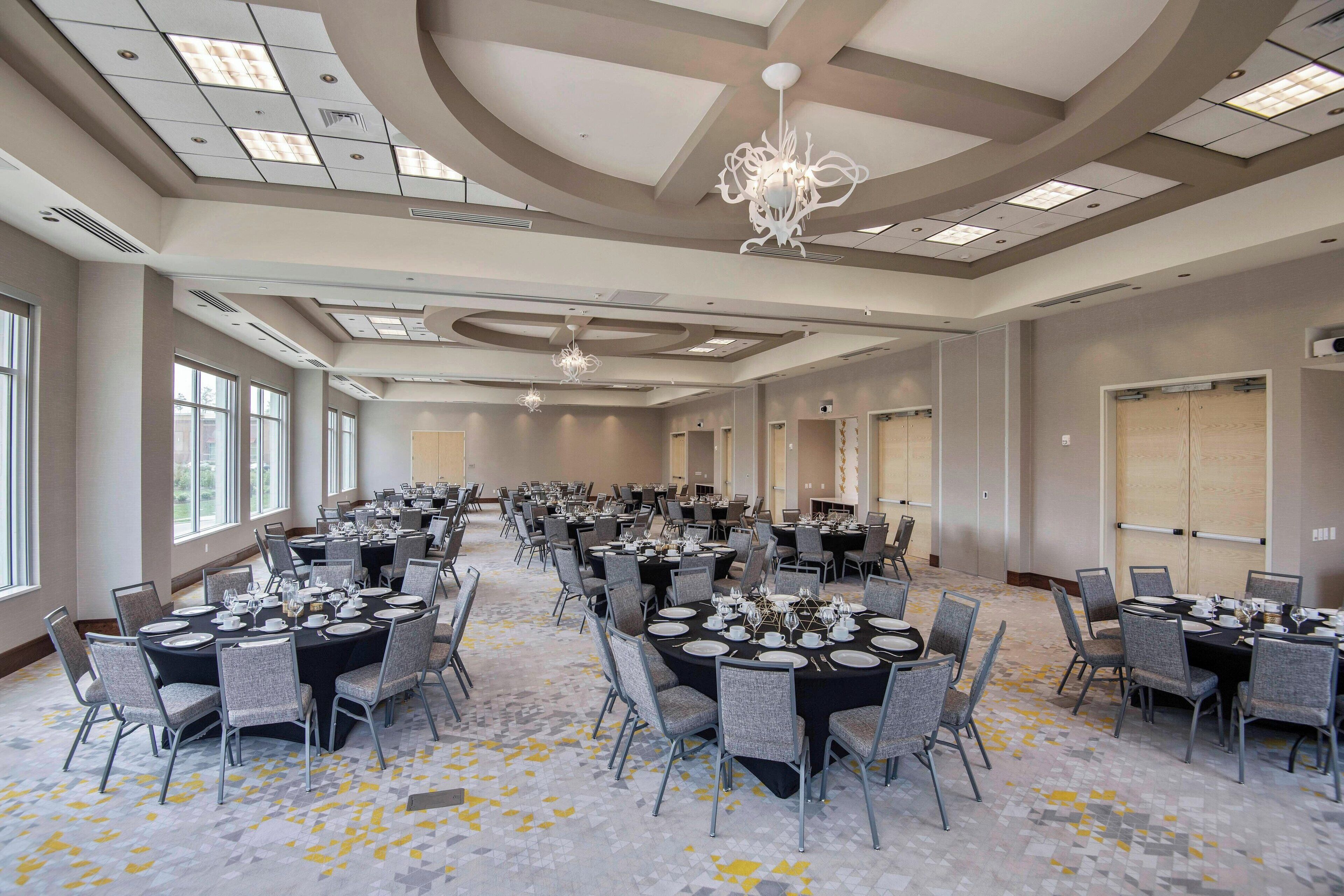 A large conference room with multiple round tables set for dining, equipped with chairs and table settings.