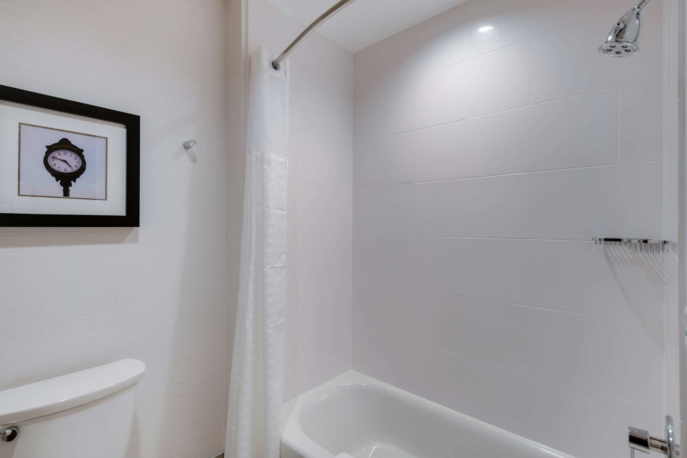 A bathroom with a white bathtub, a framed clock on the wall, and a toilet.