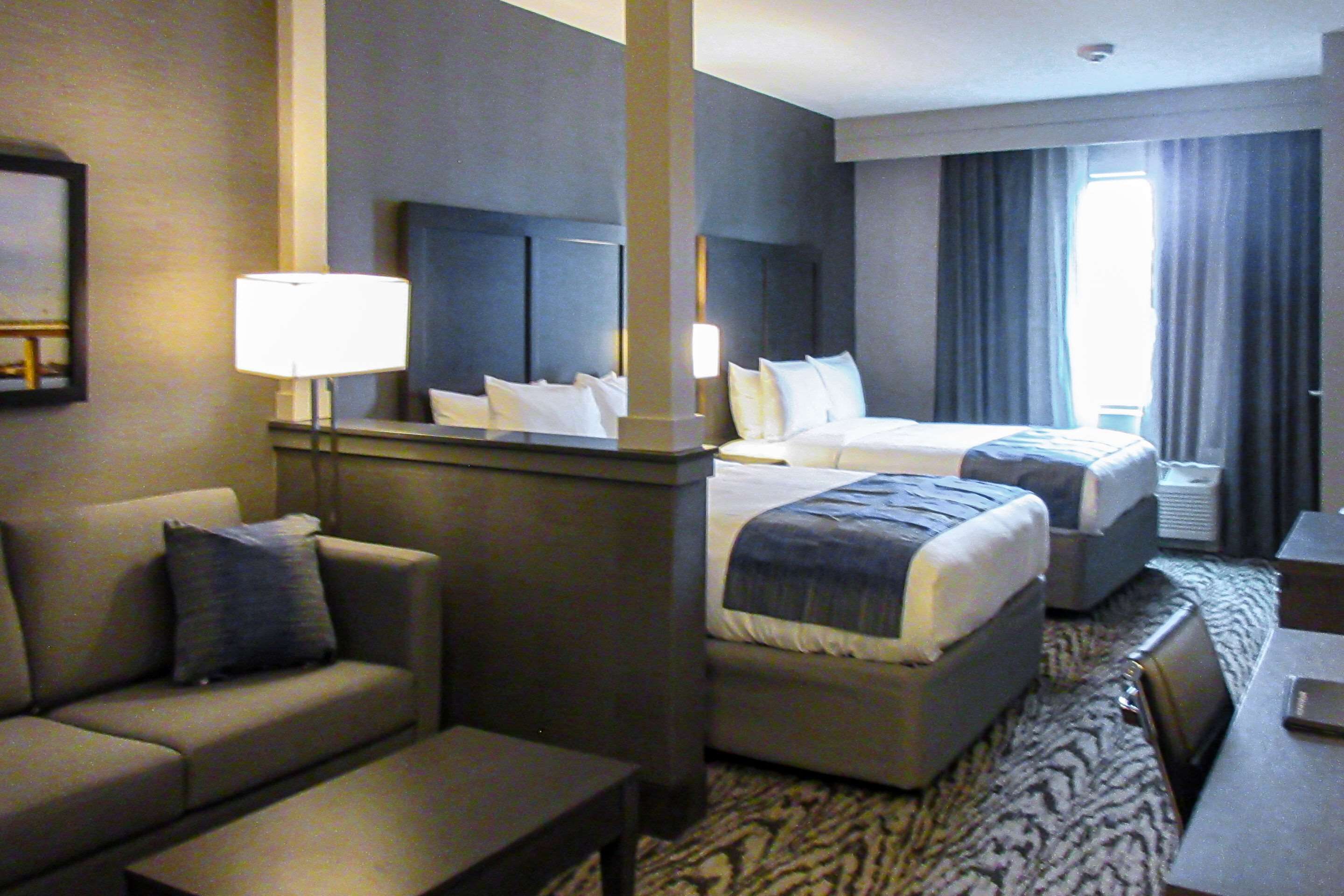 A hotel room with a sofa, two beds, a desk, and a large window with curtains.