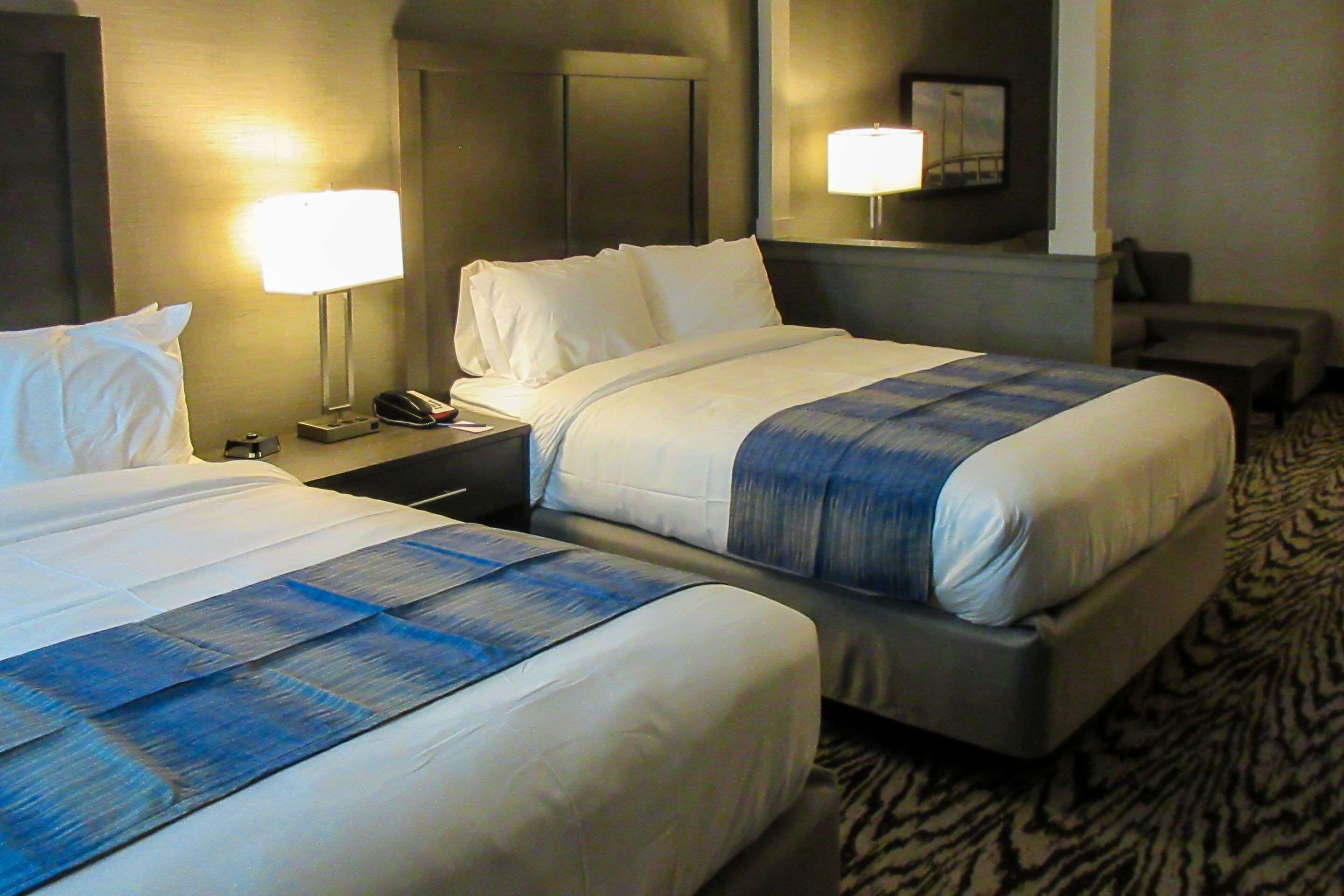 A hotel room with two beds, a nightstand with a lamp, a telephone, and a wall-mounted picture.