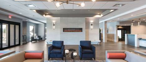 Een ruime lobby met moderne meubels, een centraal hanglamp en een receptiebalie.