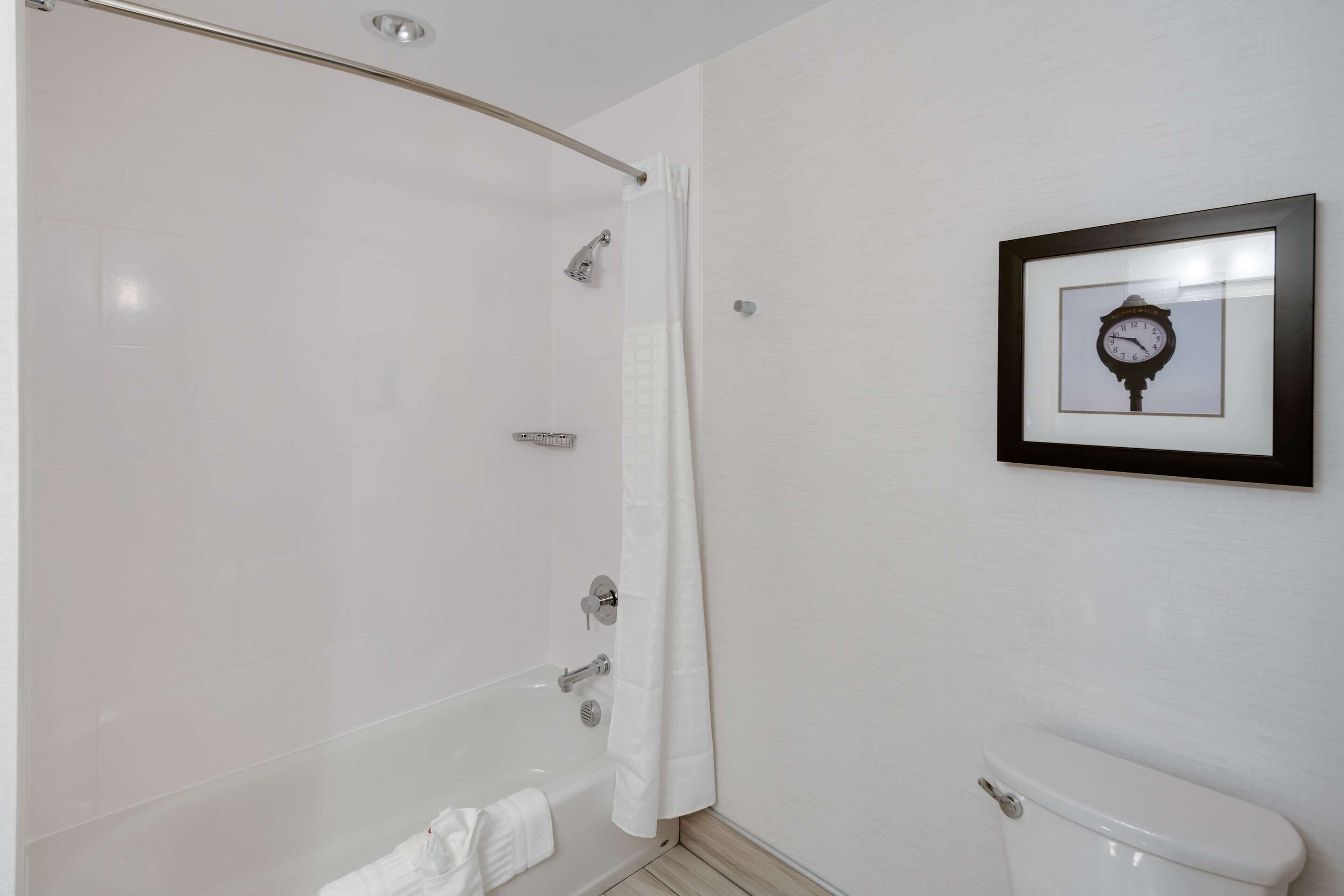 Un bagno con una vasca, un water e una cornice con un orologio appeso al muro.