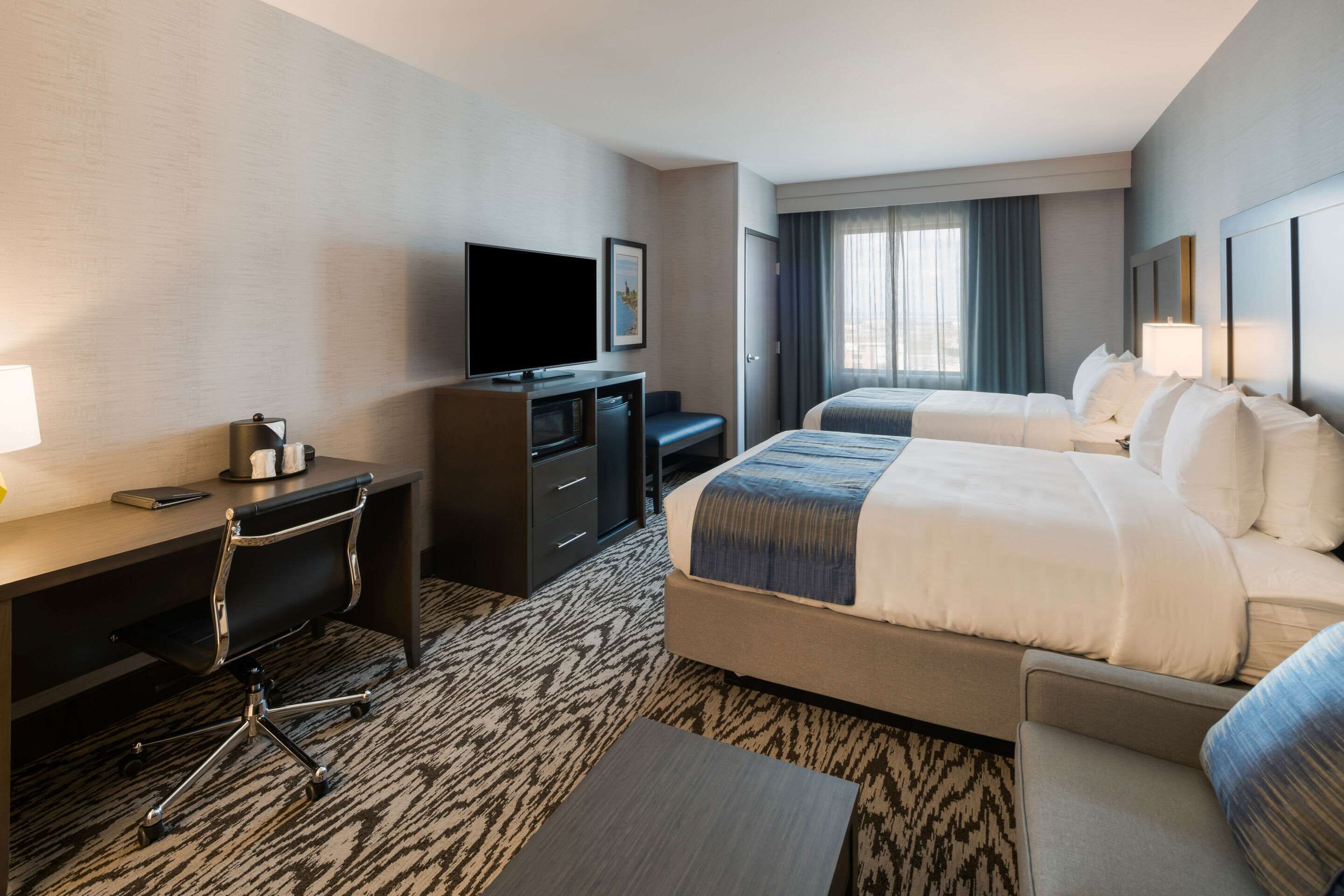 A hotel room with a bed, a desk with a television, a chair, and a small table.
