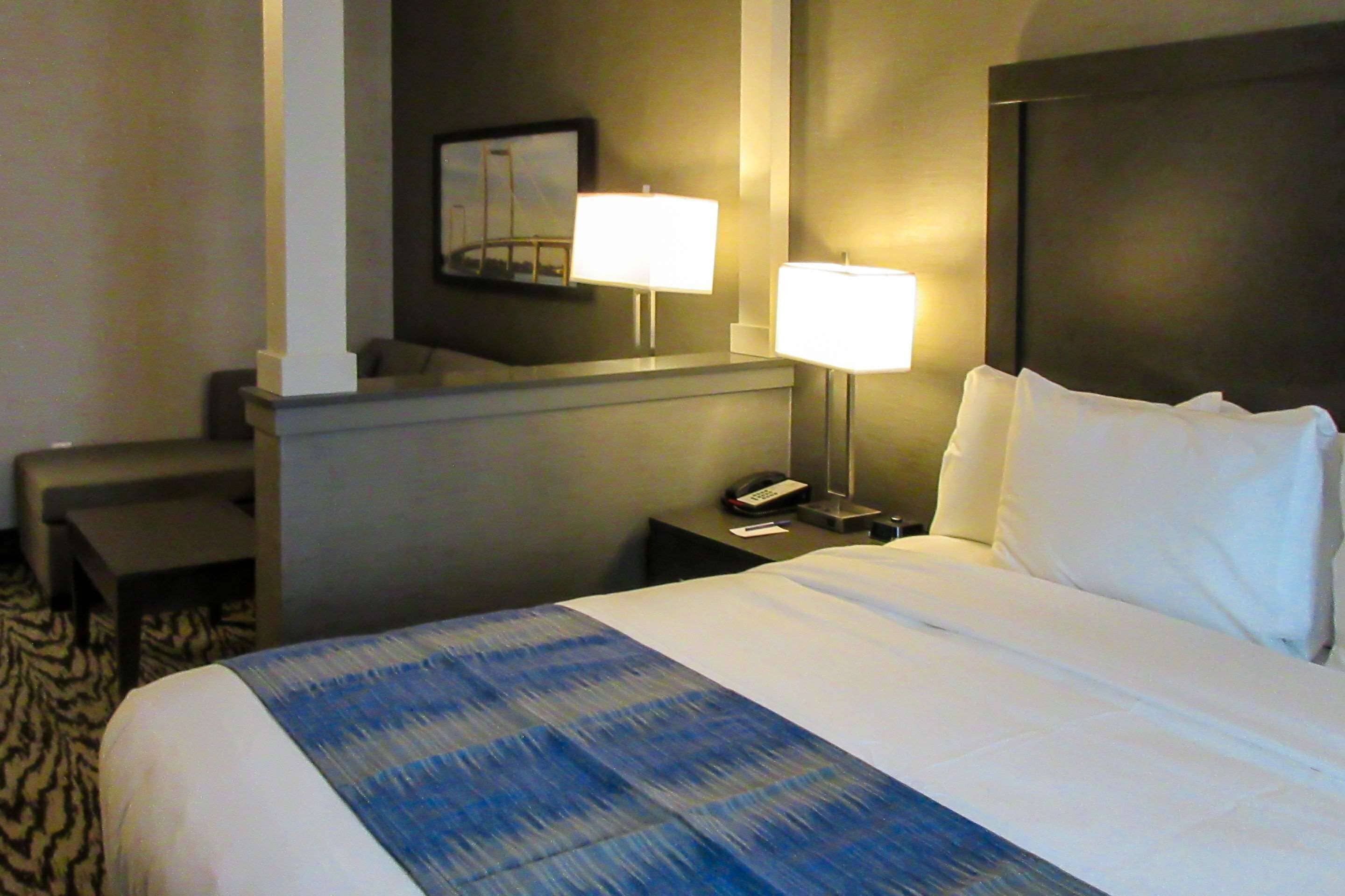 A hotel room with a large bed, a desk, a chair, and two bedside lamps.