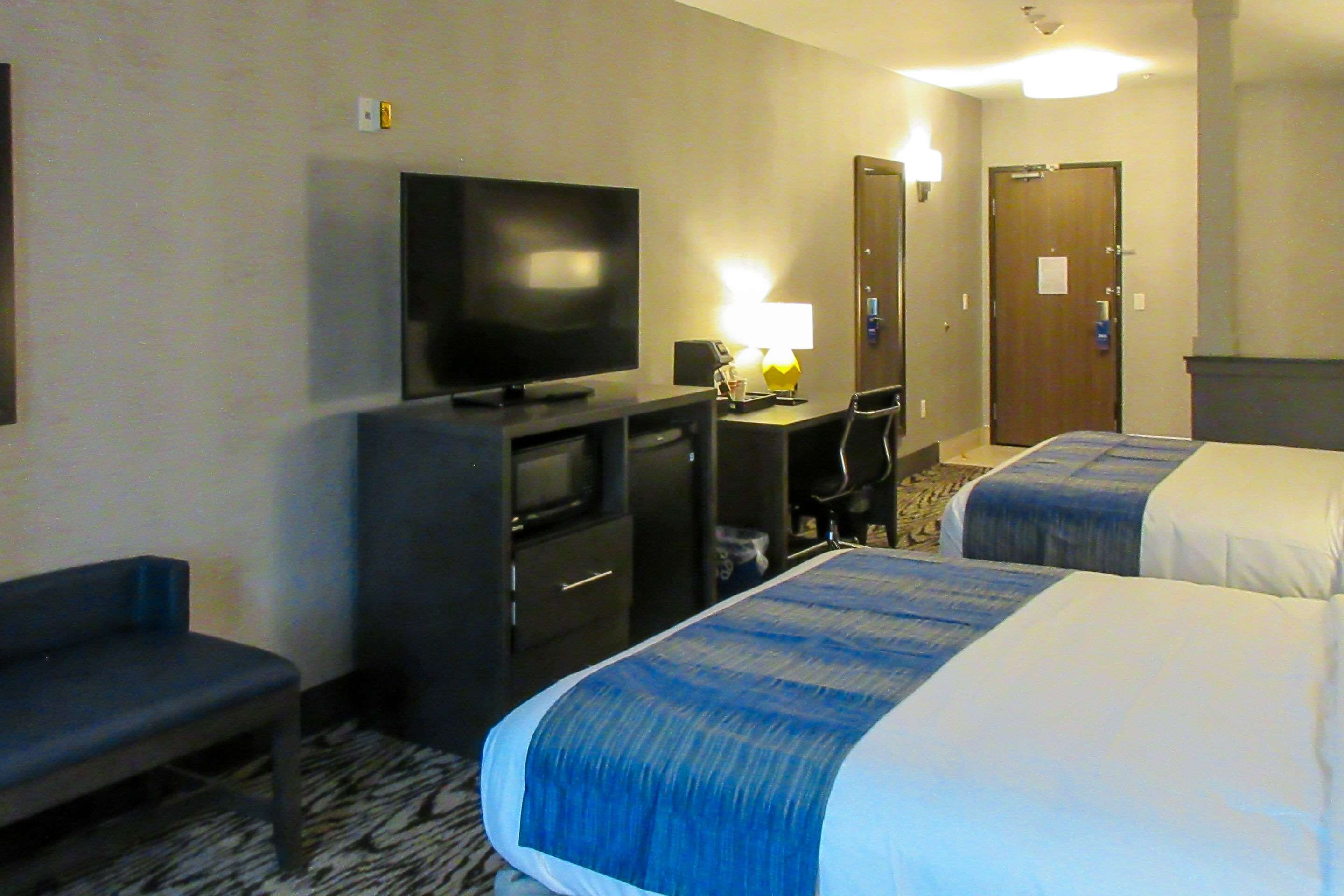 Ein Hotelzimmer mit Fernseher, Schreibtisch, Stuhl und zwei Betten.