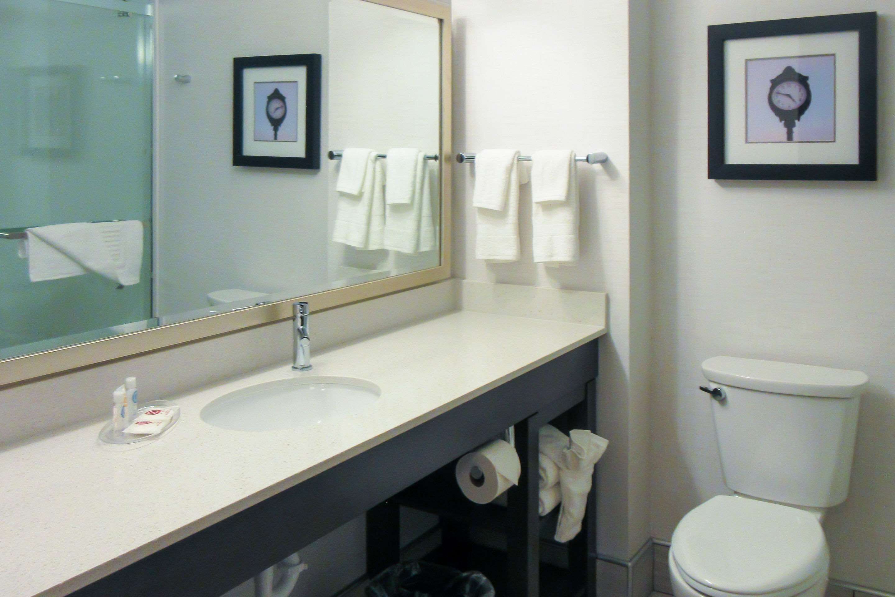 A bathroom with a sink, mirror, toilet, and framed pictures on the wall.