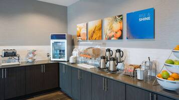 A modern kitchen with dark cabinets, a coffee station, and a fruit bowl.