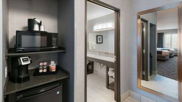 A hotel room with a microwave, coffee maker, and a small refrigerator. There is a mirror reflecting the room and a door leading to another room.