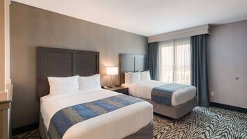 Una habitación de hotel con dos camas, una mesita de noche con lámpara y un ventanal con cortinas.